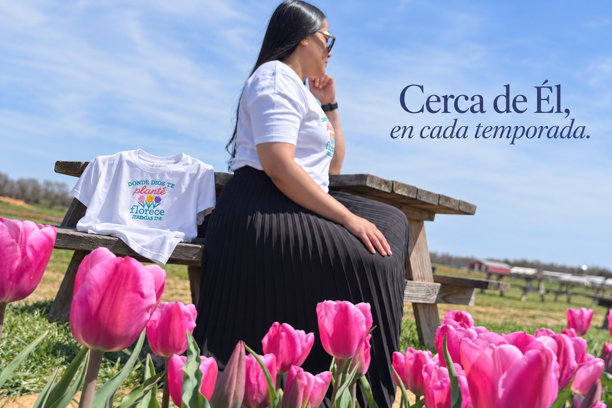 Cerca de Él, en cada temporada. Jennifer entre tulipanes y camiseta Donde Dios te planté florece sobre el banquito.