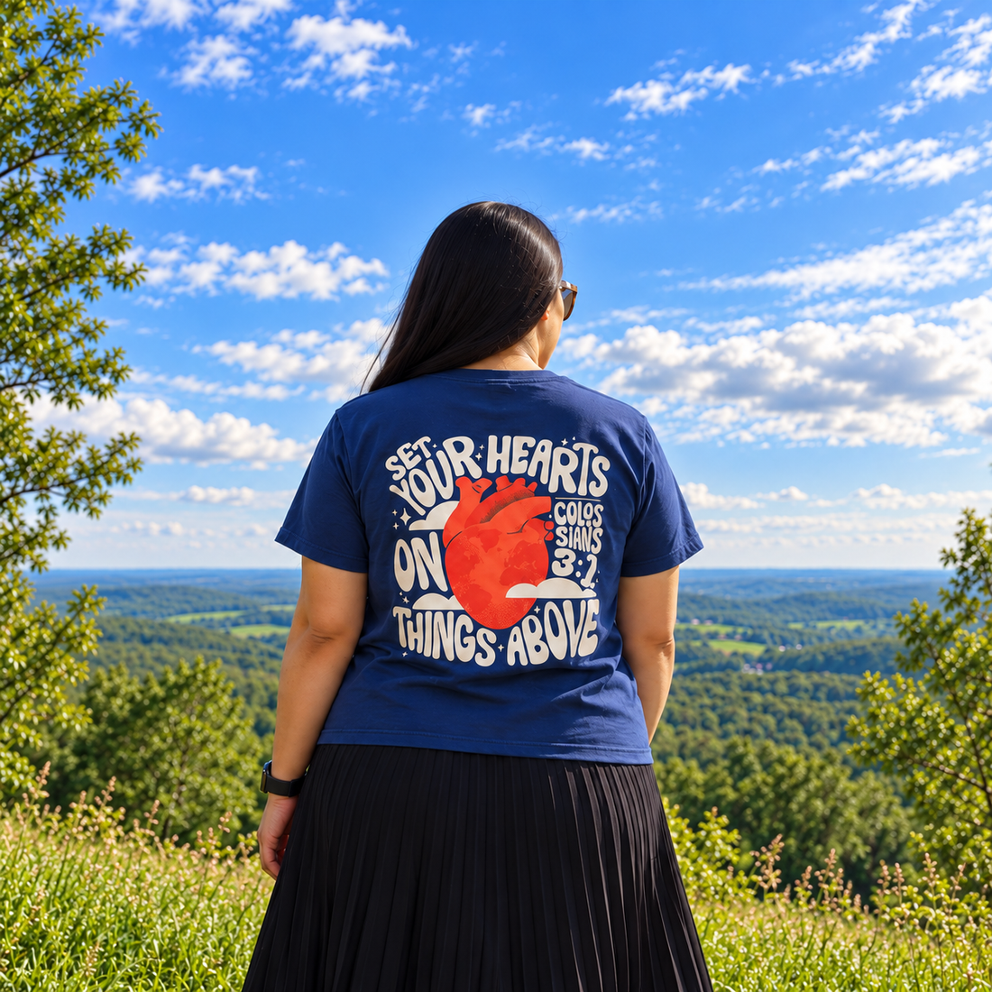 Jennifer de espalda con la camiseta Mirada en lo eterno, contemplando el cielo y un paisaje natural.